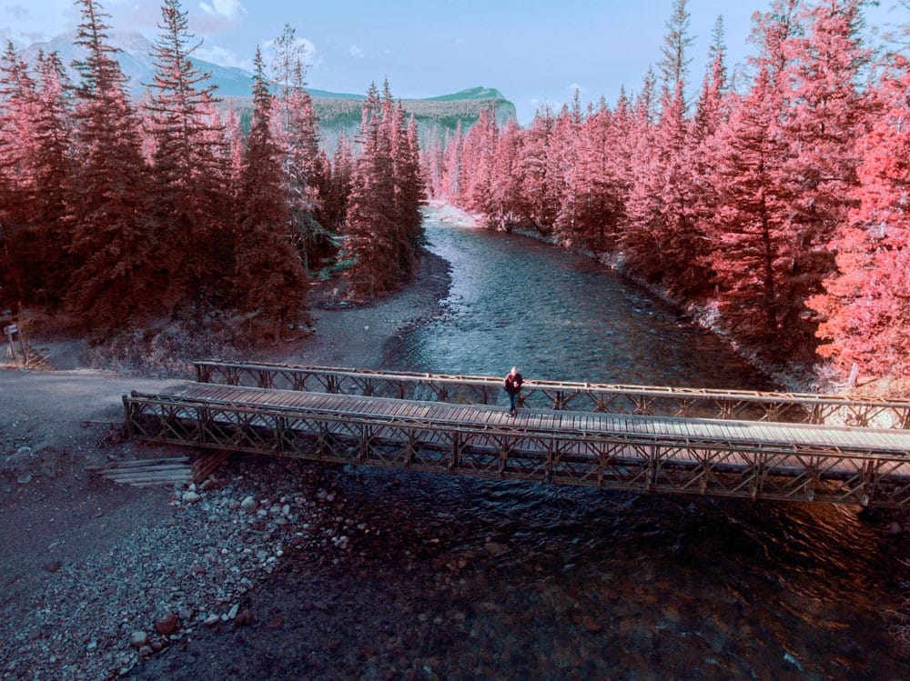Jasper Canadá fotografía aérea de un lago con los árboles rojos alrededor y un hombre en medio de un puente